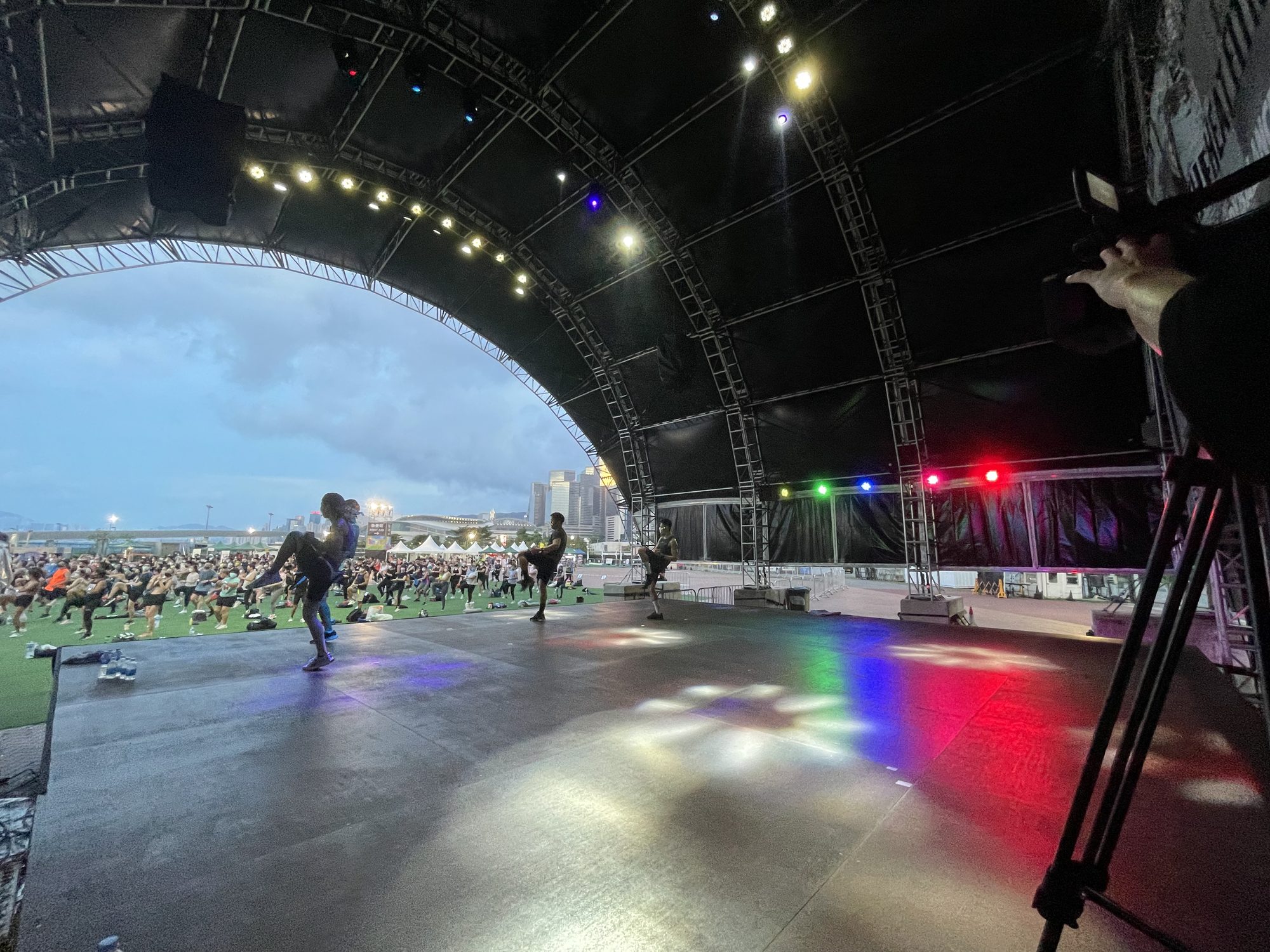 Camera at stage right covering an outdoor session, with the crowd and city skyline beyond the stage